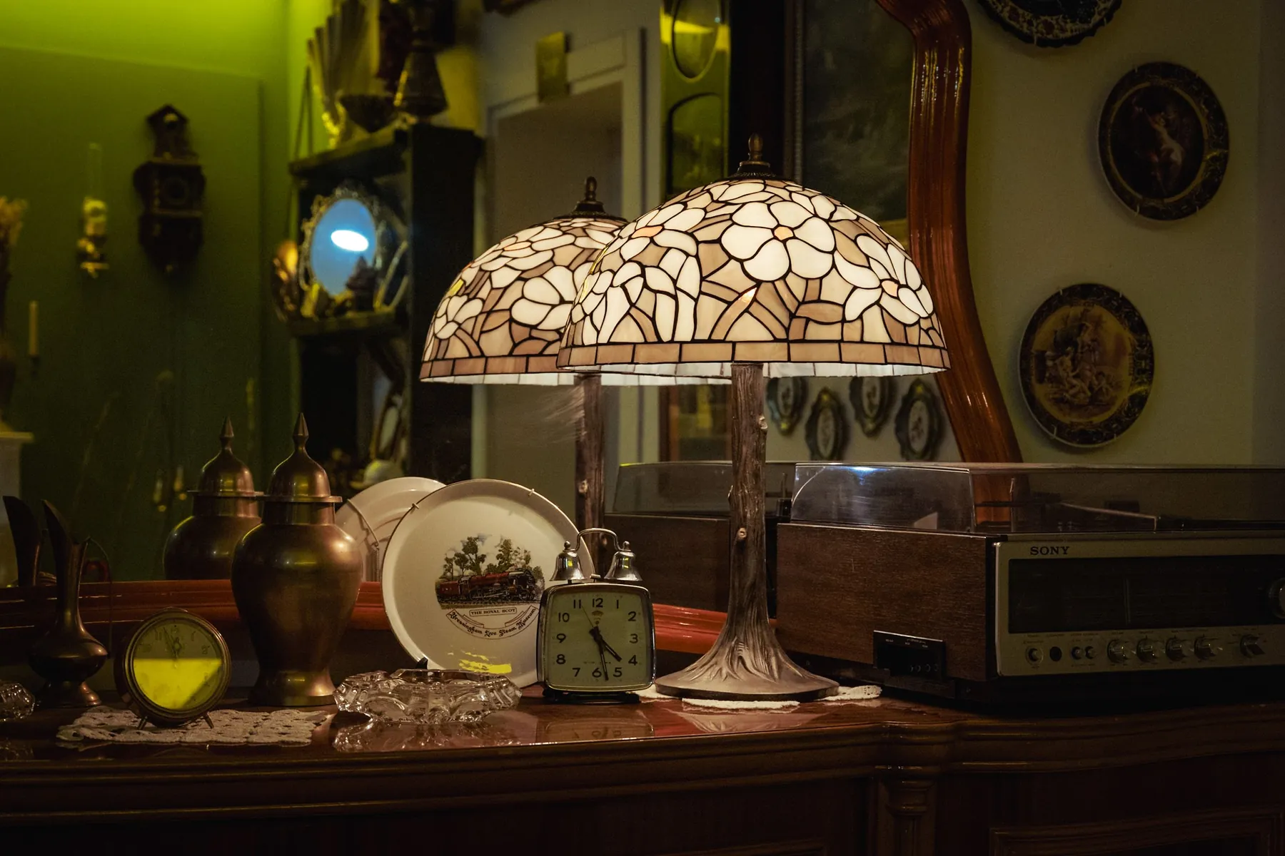 A wooden sideboard styled with a vintage radio, glass and ceramic vases, a brass lamp and a row of records